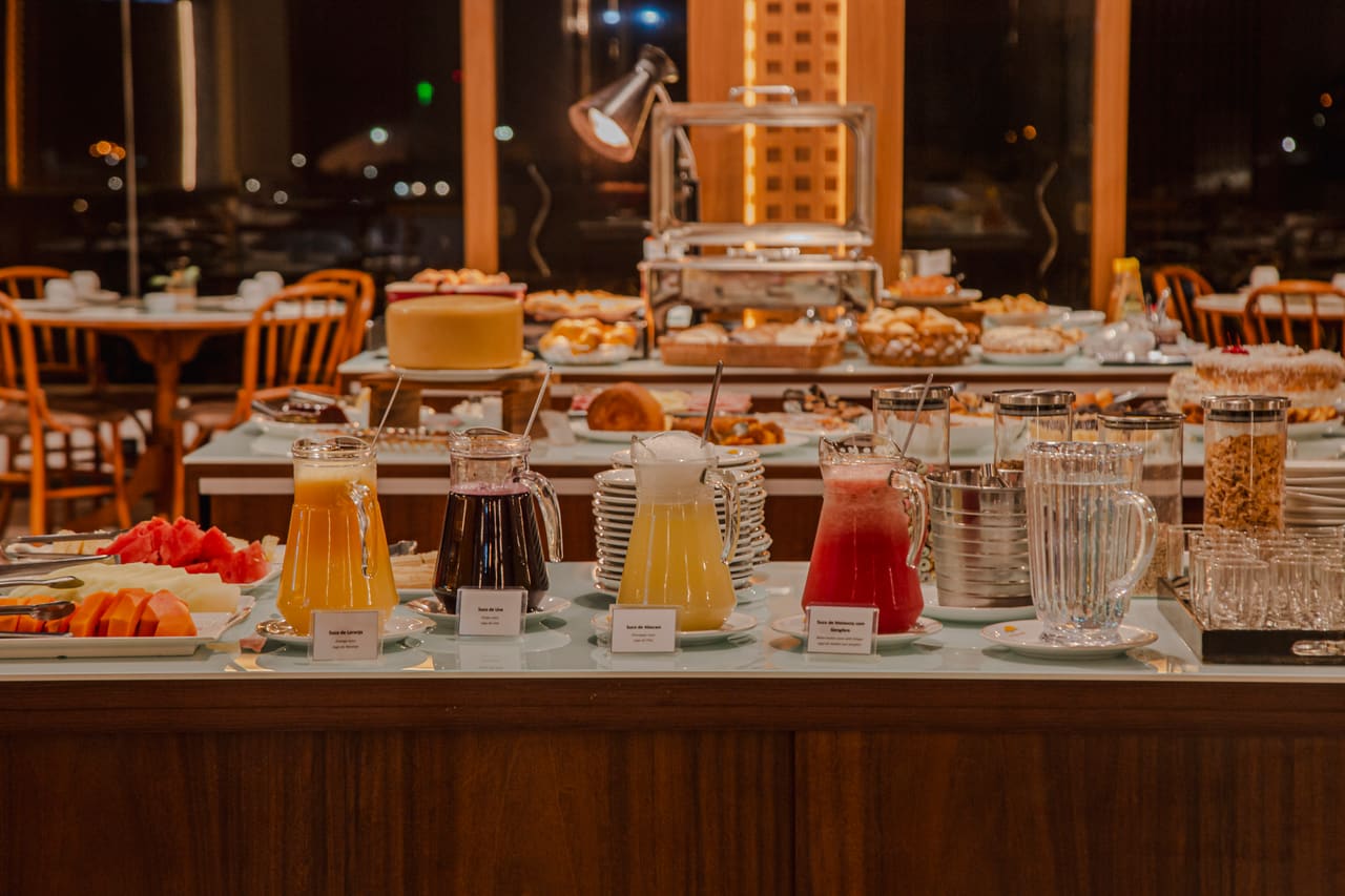 Buffet de café da manhã com jarras de suco, bolos e rechauds