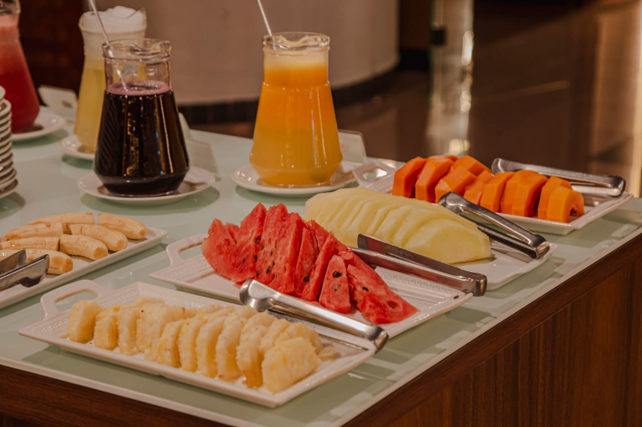 Frutas fatiadas — melancia, mamão, abacaxi e melão — e jarras de suco