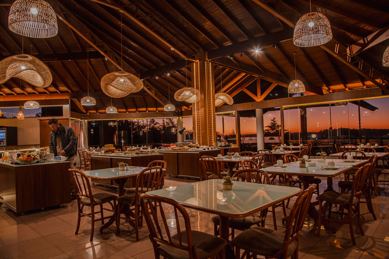 Restaurante ao entardecer com mesas postas e pôr do sol pelas janelas